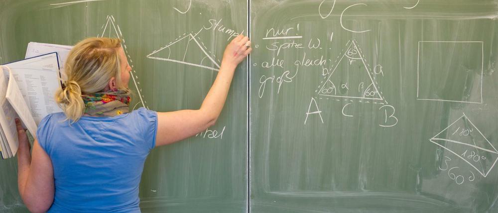  Eine Lehrerin schreibt mit Kreide an die Tafel. 