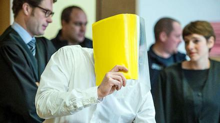 Hinter diesem gelben Hefter verbirgt der mutmaßliche "Maskenmann" im Gerichtssaal sein Gesicht.