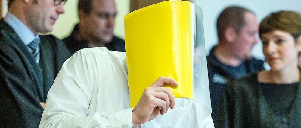 Hinter diesem gelben Hefter verbirgt der mutmaßliche "Maskenmann" im Gerichtssaal sein Gesicht.