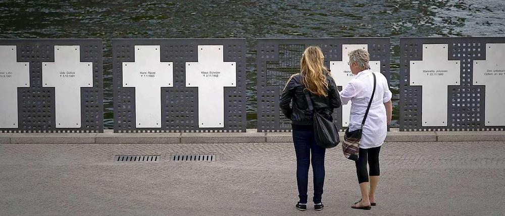 Touristen stehen im Regierungsviertel in Berlin vor Kreuzen zum Gedenken an Maueropfer. Der Bau der Berliner Mauer jährt sich am Freitag zum 49. Mal.