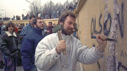 Ein Mann steht mit Hammer und Meißel an der Berliner Mauer und schlägt einen Brocken heraus.