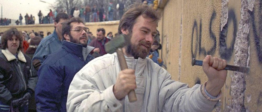 Ein Mann steht mit Hammer und Meißel an der Berliner Mauer und schlägt einen Brocken heraus.