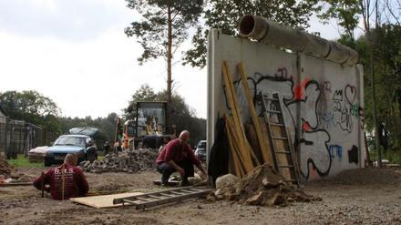 Was von der Berliner Mauer noch steht. Arbeiter sanieren das Stück; links hinter dem Zaun befindet sich Berlin-Spandau, der Ortsteil Kladow.