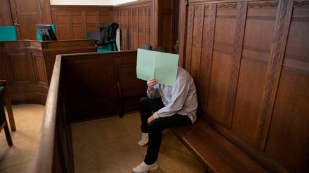 Der Angeklagte hält sich in einem Gerichtssaal im Landgericht ein Papier vor sein Gesicht. 