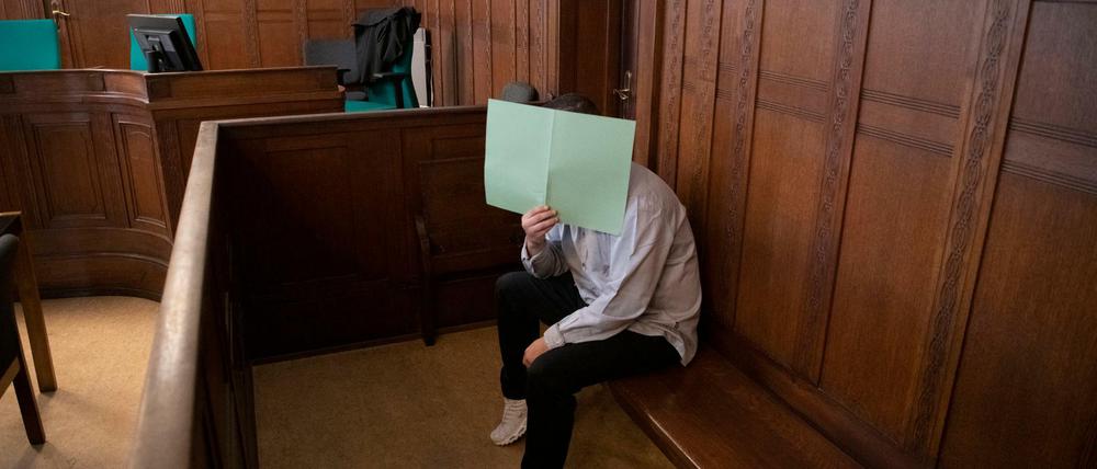 Der Angeklagte hält sich in einem Gerichtssaal im Landgericht ein Papier vor sein Gesicht. 