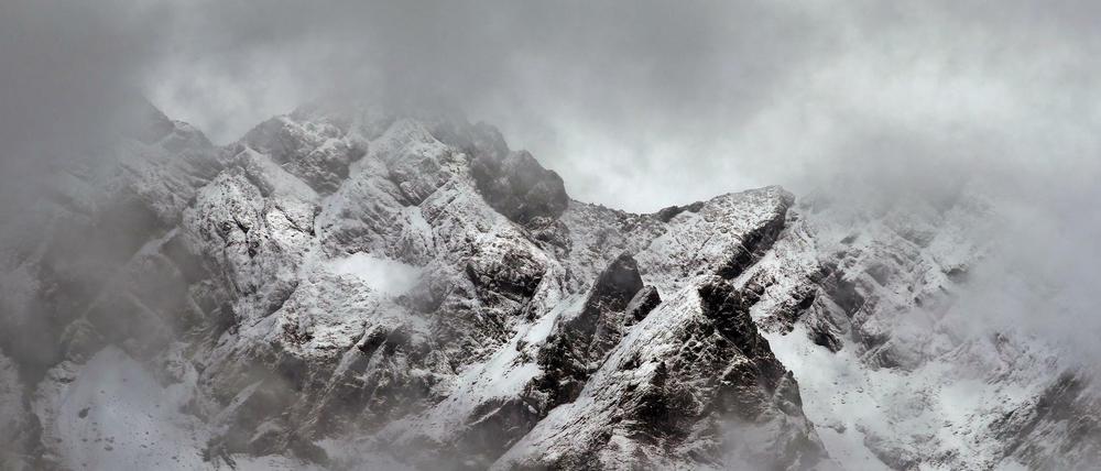 Die verschneiten Alpen sind durch eine Wolkenlücke zu sehen.