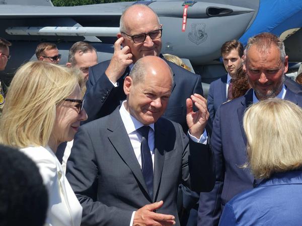 Bundeskanzler Olaf Scholz und Brandenburgs Ministerpräsident Dietmar Woidke (beide SPD) gestikulieren vor einem US-Kampfjet. Links in weiß: Amy Gutmann, die Botschafterin der USA.