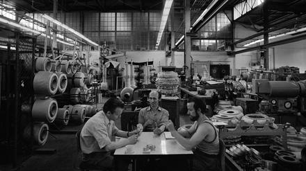 Drei Männer sitzen sehr entspannt in einer riesigen Werkhalle des Transformatorenwerks Oberschöneweide und spielen Karten.