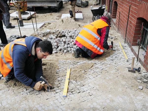 Steinsetzer bei der Arbeit in der Pappelallee, deren ursprünglicher Gehweg nach Straßenbauarbeiten wiederhergestellt wurde.