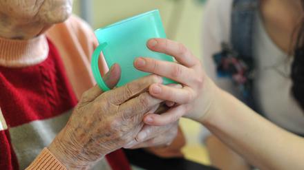 Eine Pflegekraft hilft einer alten Frau in Frankfurt (Oder) beim Trinken aus einem Becher in einem Seniorenheim.