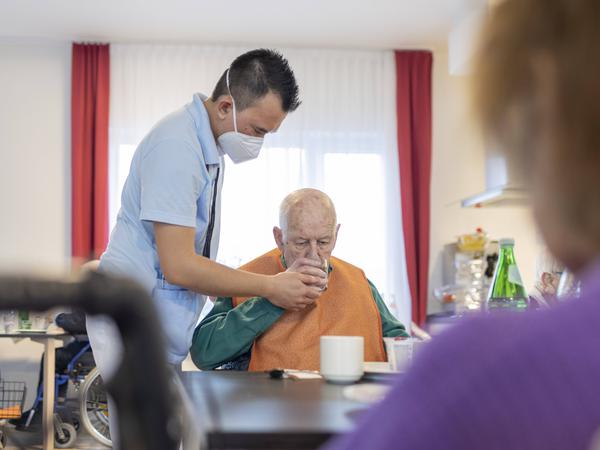 Pfleger hilft einem Mann im Pflegeheim beim Trinken (Symbolbild).