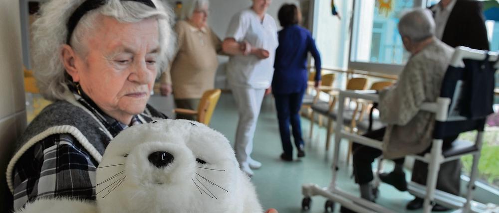 Eine Demenzkranke hält einen Roboter mit Robbenfell in der Hand und streichelt ihn.
