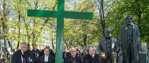 Evangelische und katholische Würdenträger passieren bei der Karfreitagsprozession das Denkmal von Marx und Engels.