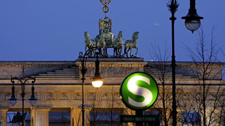Quadriga auf dem Brandenburger Tor vor Abendhimmel. Im Vordergrund das S-Bahnsymbol am unterirdischen Bahnhof Unter den Linden.