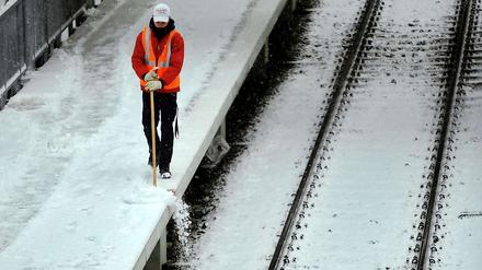 Ein S-Bahn-Mitarbeiter fegt am Dienstag Schnee vom Bahnsteig des S-Bahnhofs Ostkreuz. In der Nacht zu Mittwoch hat es erneut geschneit.