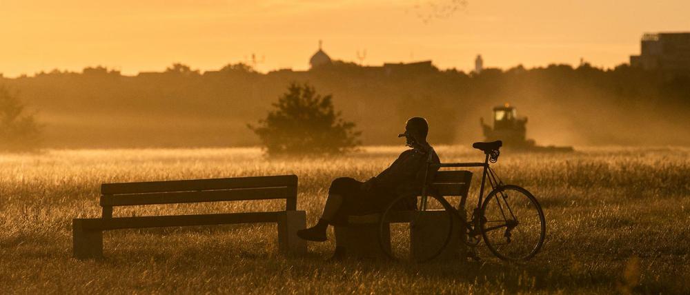 Ein Mann genießt auf dem Tempelhofer Feld die Morgenstimmung im Licht der aufgehenden Sonne. 