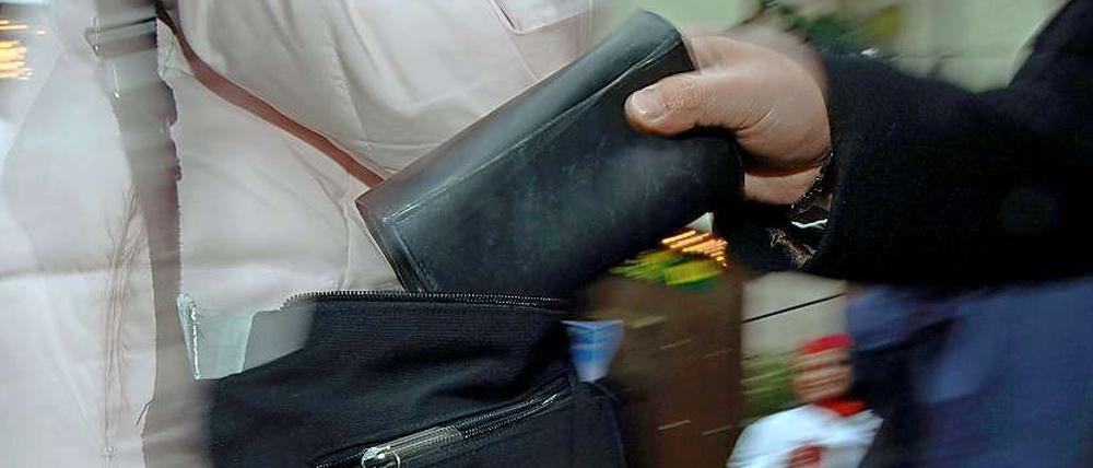 Ein Taschendieb zieht eine Geldbörse aus einer Handtasche.