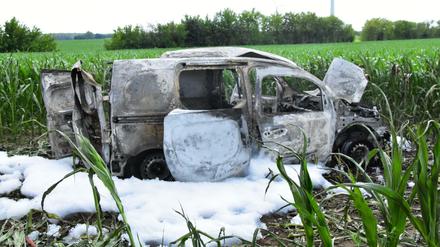 Ein ausgebranntes Auto steht in einem Feld, umgeben von Löschschaum. In dem Auto ist eine Leiche entdeckt worden.