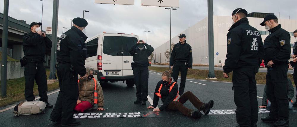 Bundespolizisten stehen am Flughafen BER vor Klimaschutz-Aktivisten der Initiative "Aufstand der letzten Generation", die eine Zufahrt zum Hauptstadt-Flughafen BER blockieren.