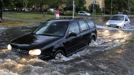 Berlin: Mehrere Autos fahren nach schweren Regenfällen über eine teilweise überflutete Straße.