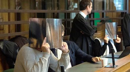 Zwei der Angeklagten sitzen neben ihren Anwälten im Gerichtssaal und verdecken ihre Gesichter.