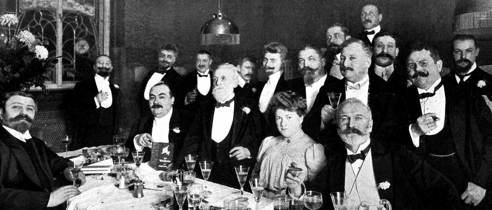 Eine festlich gekleidete Gesellschaft, bis auf die Frau des Gastgebers allesamt Herren, hat sich 1907 beim Hotelier Carl Kohlis versammelt. 