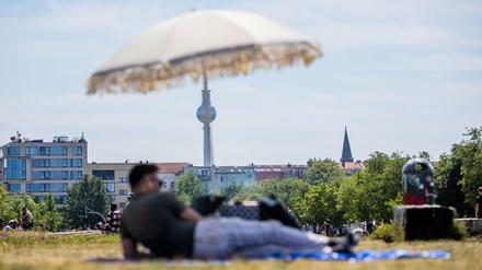 Ein Mann liegt im Mauerpark vor dem Berliner Fernsehturm unter einem Sonnenschirm (Symbolbild). 