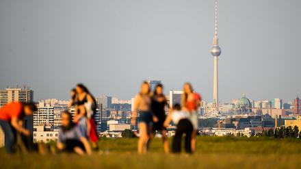 Menschen genießen vor dem Berliner Fernsehturm einen sonnigen Abend auf dem Drachenberg.
