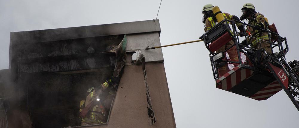 Feuerwehrmänner lösen die Verkleidung am Dach eines Hauses. Die Feuerwehr löschte einen Wohnungsbrand im Stadtteil Kreuzberg. 