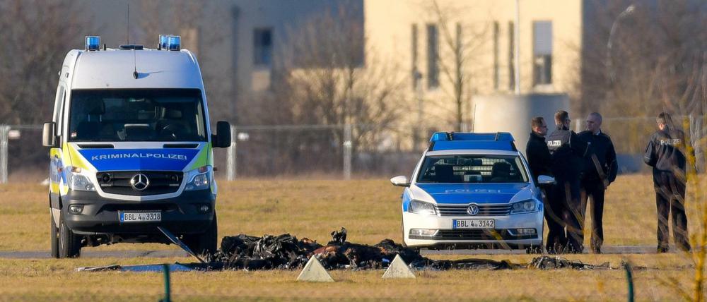Flugzeugabsturz in Strausberg: Zwischen zwei Fahrzeugen der Polizei sind die verkohlten Reste eines Kleinflugzeuges zu sehen.
