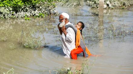 A man wades through flood waters carrying his grand daughter on his back following rains and floods during the monsoon season in Charsadda, Pakistan August 28, 2022. REUTERS/Fayaz Aziz