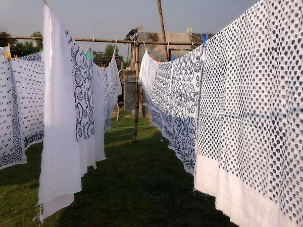 Weiße Leinentücher, die mit Indigo-Mustern bedurckt sind, hängen auf einer Wäscheleine in einem Dorf in Bangladesch