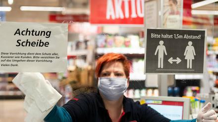 Ein Mitarbeiterin in einem Supermarkt in Dresden putzt vor Ladenöffnung eine Plexiglasscheibe, einen sogenannten "Spuckschutz", an der Kasse.