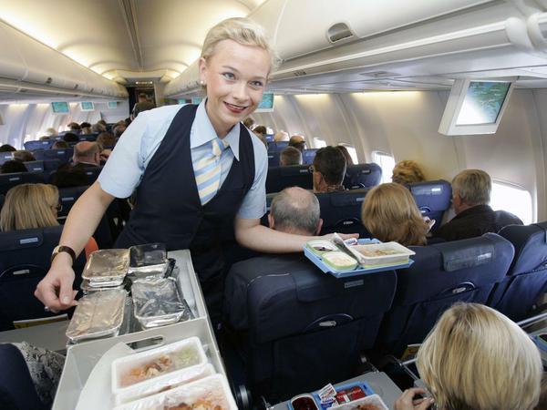 Eine Flugbegleiterin verteilt Menüs an Fluggäste in einem Passagierflugzeug.
