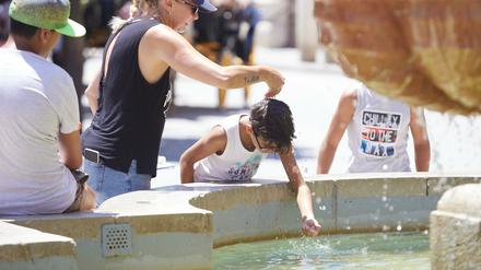 Eine Mutter gießt während einer Hitzewelle ihrem Sohn Wasser über den Kopf am Brunnen auf dem Platz Virgen de los Reyes in Sevilla. Foto: dpa/Joaquin Corchero/EUROPA PRESS