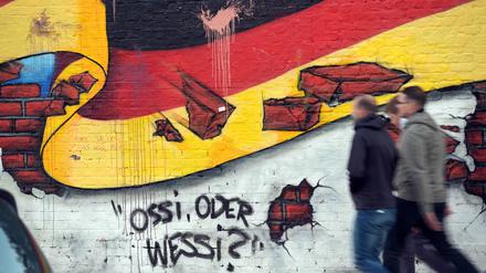 Passanten gehen an einem Wandbild von Caspar Kirchner mit der deutschen Nationalflagge und dem Schriftzug „Ossi oder Wessi?“ vorbei (Symbolbild).