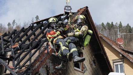 Zwei Feuerwehrleute werden mit Hilfe einer Drehleiter aus dem ausgebrannten Dachstuhl herausgehoben.