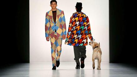 Zwei männliche Models laufen mit Hunden über den Laufsteg