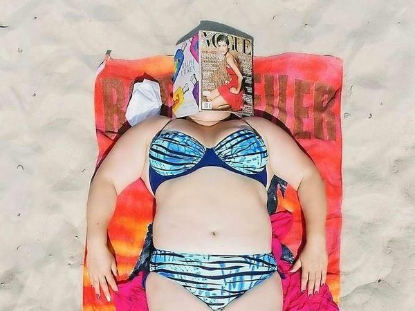 Eine mollige Frau liegt im Bikini auf einem bunten Strandtuch. Sie schläft und hat sich eine Vogue über das Gesicht gelegt-
