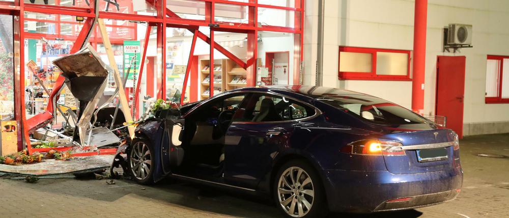 Ein Tesla steht nach einem Unfall vor dem zerstörten Eingang eines Baumarktes.