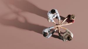 Vier Menschen stehen im Kreis, ihre ausgestreckten Hände treffen sich in der Mitte.