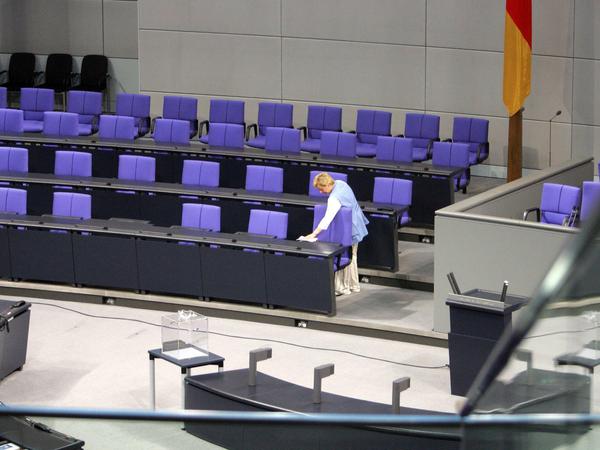 Eine Putzfrau reinigt den Platz von Bundeskanzlerin Angela Merkel im Bundestag.  