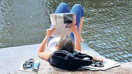 Eine junge Frau liest Zeitung am Berliner Landwehrkanal. 