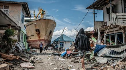 Indonesien, Palu: Menschen gehen eine Straße entlang in der Nähe des Ortes, wo ein Schiff während des Tsunamis an Land gespült wurde. Rund 5000 Menschen werden nach den Erdbeben und dem Tsunami in Indonesien noch immer vermisst. 