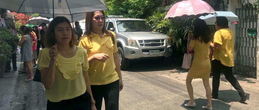Passanten sind in gelber Kleidung auf einer Straße in Thailands Hauptstadt Bangkok unterwegs.