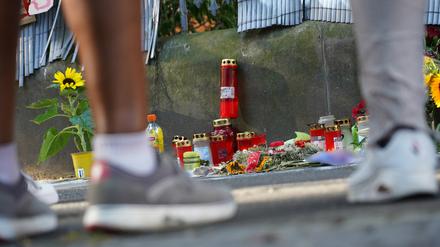 Menschen stehen vor einem Zaun, an dem mit Kerzen und Blumen eines von der Polizei erschossenen Jugendlichen gedacht wird. 