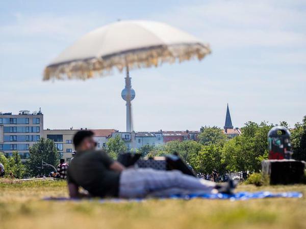 Ein Mann liegt im Mauerpark vor dem Berliner Fernsehturm unter einem Sonnenschirm. 