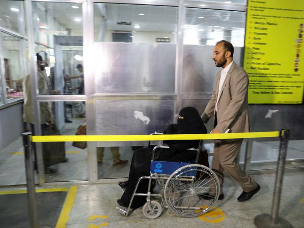 Ein Mann hilft einer Verwandten im Rollstuhl in der Abflughalle am Flughafen Sanaa.