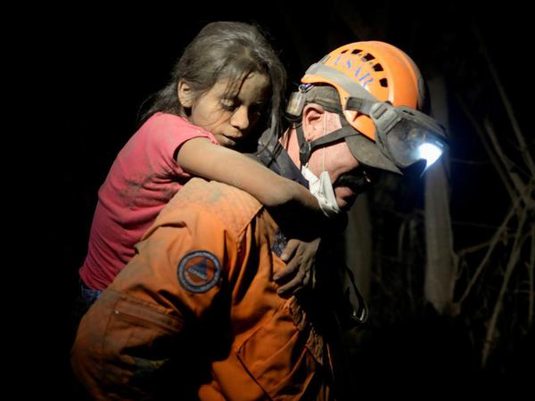 Ein Rettungshelfer trägt ein mit Asche bedecktes Kind.