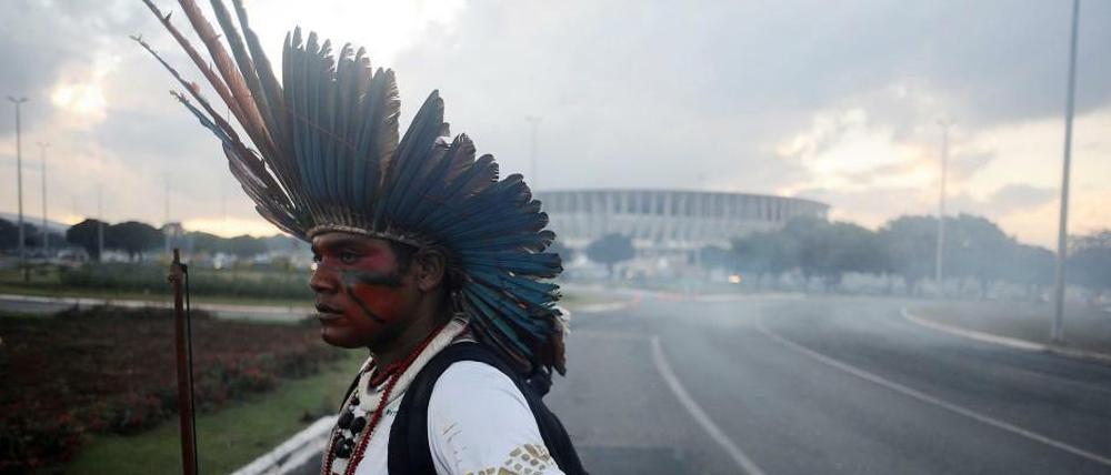 Ein Demonstrant im Federschmuck der Ureinwohner Brasiliens steht vor dem neuen Stadion, dessen Baukosten sich immens gesteigert haben.